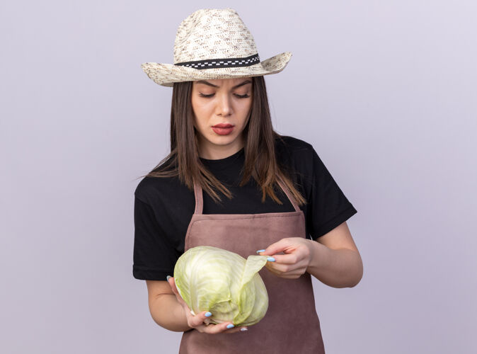 花园自信漂亮的白人女园丁戴着园艺帽拿着白菜看着漂亮帽子卷心菜