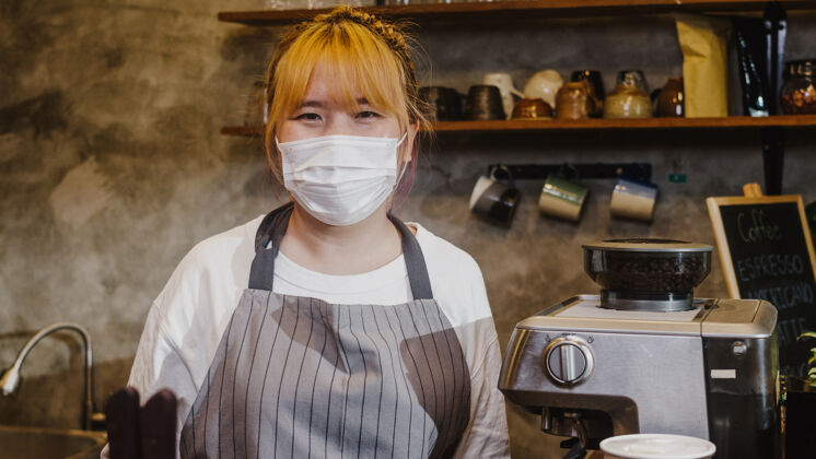 餐厅肖像年轻的亚洲女孩女服务员戴着医用面罩 在市区咖啡馆被关后 心情愉快地微笑着等待客人日本人自助餐厅微笑