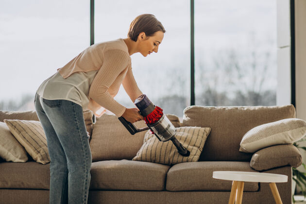 沙发年轻女子用可充电吸尘器在家清洗室内地板休闲