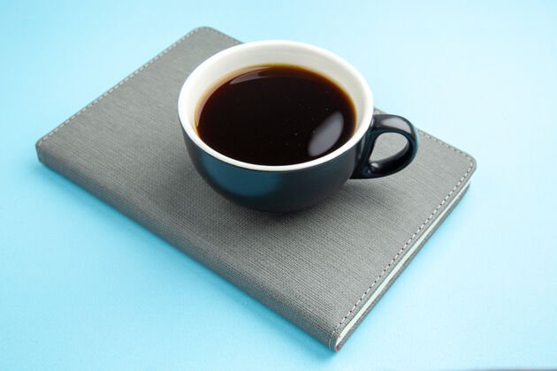 笔记本蓝色表面上的灰色笔记本上的一杯红茶的侧视图壁板杯子咖啡杯