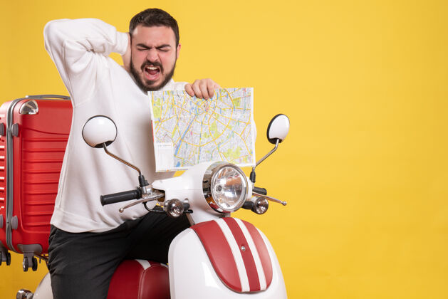 地图一个年轻的紧张不安的男人坐在摩托车上 手提箱上拿着地图 耳朵疼痛 背景是黄色的背景疼痛高尔夫