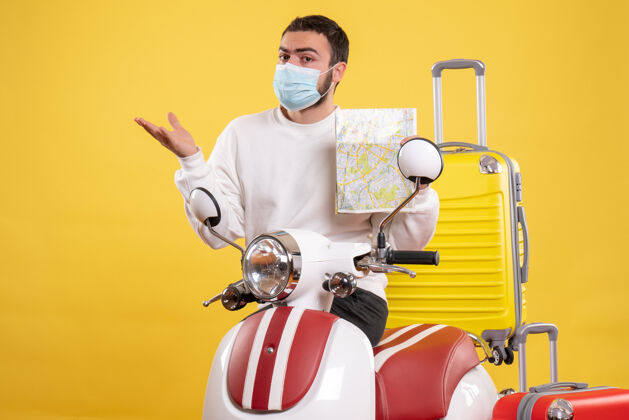 手提箱旅行概念的俯视图 戴着医用面罩的年轻人站在黄色手提箱的摩托车旁面具医疗男人