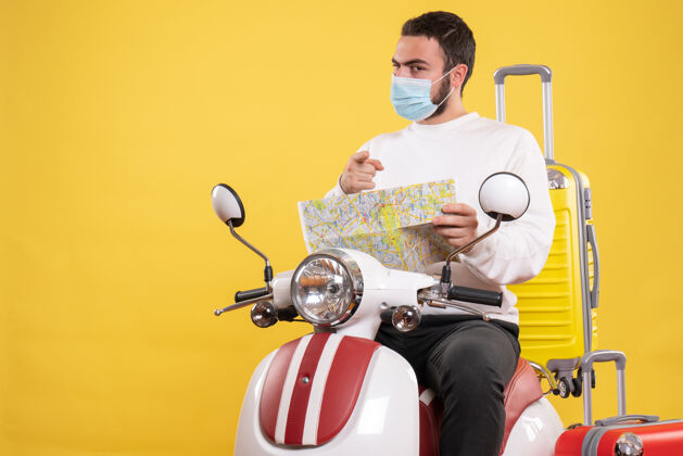 男人带着医用面罩的自信的家伙坐在摩托车上 带着黄色的手提箱 拿着黄色的地图向前看黄色人坐着