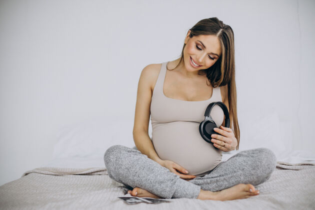 床孕妇带着超声波照片把带音乐的耳机放在肚子上保健等待父母