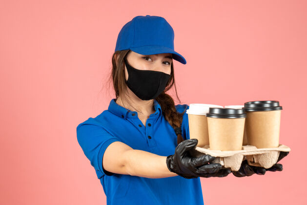 工作半身镜头的信使女孩戴着医用面罩和手套拿着咖啡粉彩桃背景身体成人一半