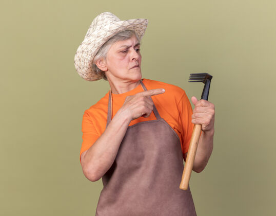 园艺严肃的上了年纪的女园丁戴着园艺帽拿着耙子看着老人帽子举行