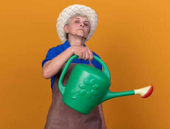 信心自信的上了年纪的女园丁戴着园艺帽拿着浇水罐浇水园艺橙色