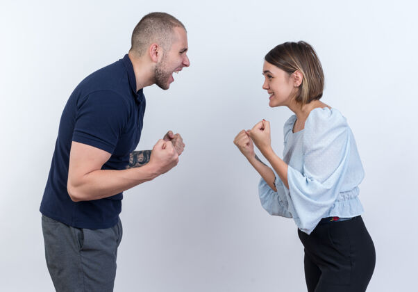 握紧年轻漂亮的夫妇站在白色的墙壁上 一男一女紧握着拳头大声吵架争吵拳头手势