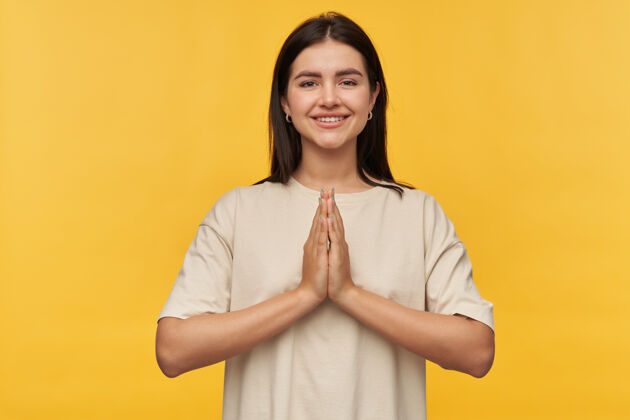 手快乐美丽的黑发年轻女子在白色T恤保持双手在黄色的墙上祈祷的立场健康禅宗平衡