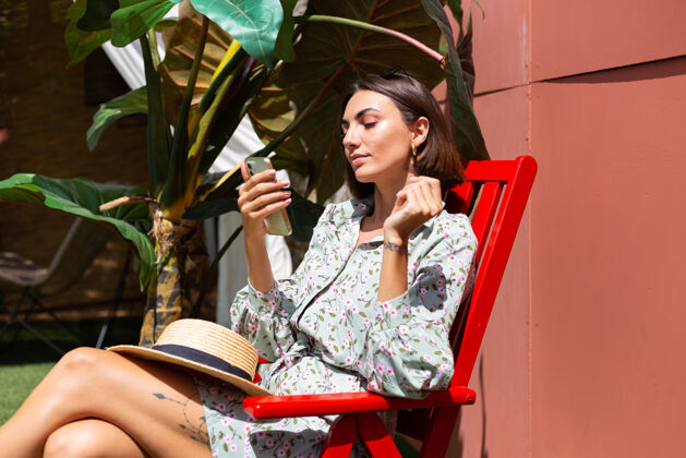 乐趣阳光明媚的日子里 穿着夏装的美女坐在后院的椅子上 手里拿着手机年轻在线异国情调