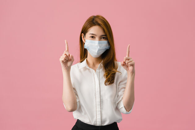 恐惧年轻的亚洲女孩戴着医用面罩 穿着休闲服 看着粉色背景上的相机 在空白处展示着一些东西社交严重背景