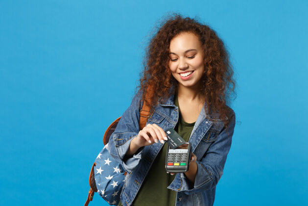 奖励年轻的非洲裔美国女孩十几岁的学生在牛仔服装 背包举行信用卡隔离在蓝色的墙上交易无现金客户