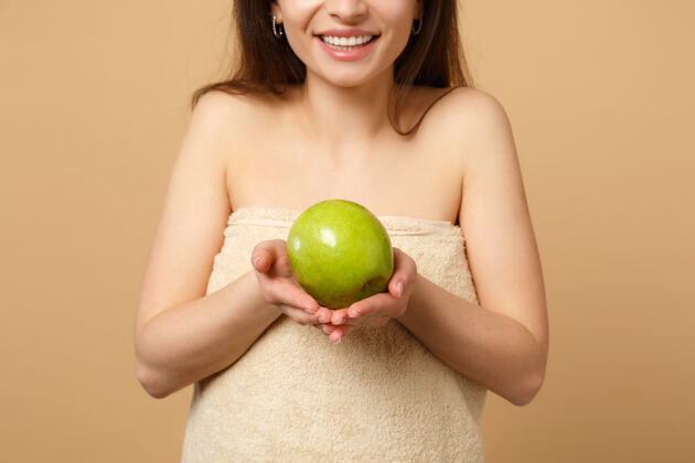 热量特写黑发半裸完美皮肤的女人 裸妆把苹果隔离在米色粉彩墙上纯净治疗苹果