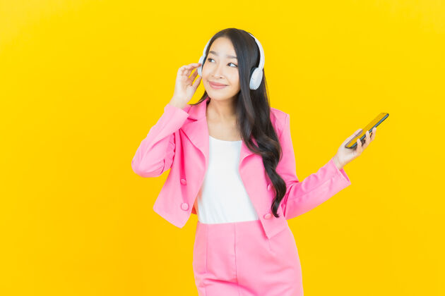 美丽画像美丽的亚洲年轻女子戴着耳机和智能手机在黄色的墙上听音乐女人青少年漂亮
