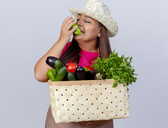 香味中年女园丁围着围裙 戴着帽子 拿着装满蔬菜的板条箱 感受着新鲜甜椒的芳香铃铛新鲜的板条箱