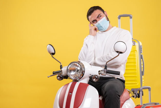 人旅行的概念与体贴的家伙在医疗面具坐在摩托车上 黄色手提箱上的黄色医疗摩托车面具