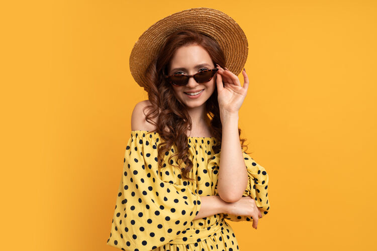 女士戴草帽戴太阳镜的红头发女人的肖像 穿着黄色的夏装趋势优雅女人