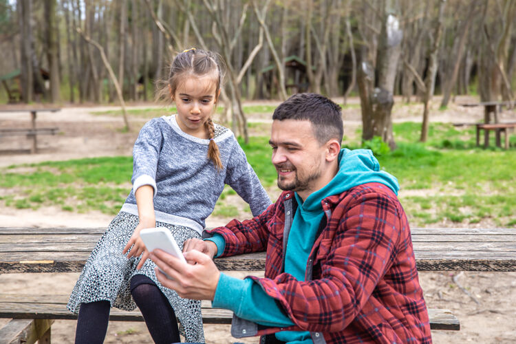 坐着爸爸和他的小女儿在树林里散步时看电话散步问题乐趣