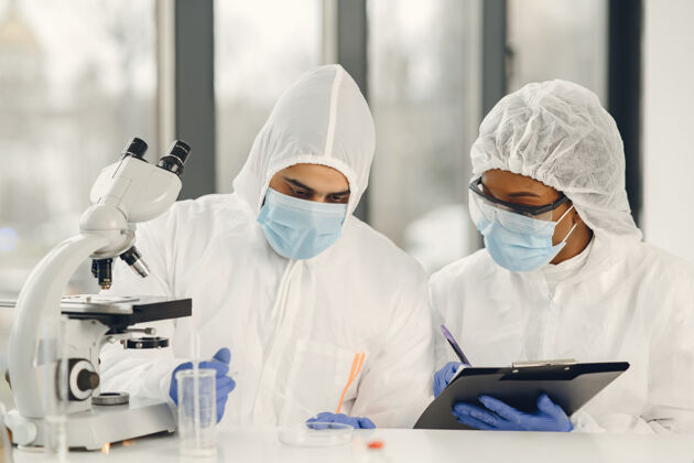 药物科学家和微生物学家穿着个人防护服 戴着口罩 在实验室里拿着试管和显微镜 寻找治疗冠状病毒感染的方法或疫苗医院化学家化学