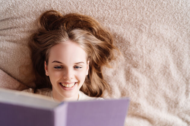女人年轻漂亮的女人在家里的床上享受着最喜欢的书休闲舒适单身