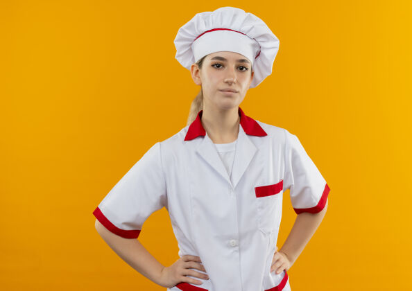腰围自信的年轻漂亮厨师穿着厨师制服 手放在腰上 隔离在橙色的墙上手自信厨师