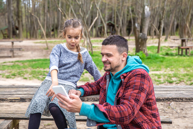 坐着爸爸和他的小女儿在树林里散步时看电话散步问题乐趣