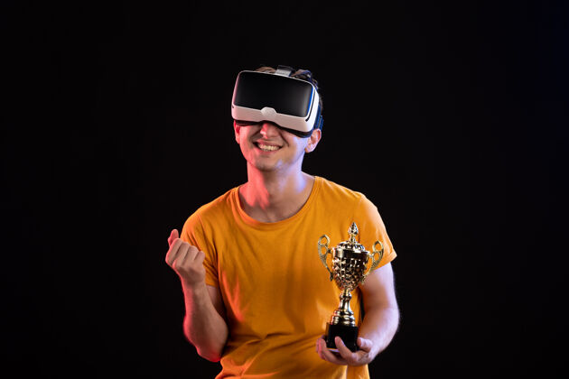 男在黑暗的墙上 年轻人拿着冠军杯玩虚拟现实的肖像黑黑杯