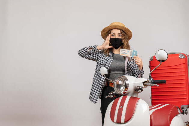 帽子一个拿着票的漂亮女人站在轻便摩托车的红色手提箱旁边面具票衣服