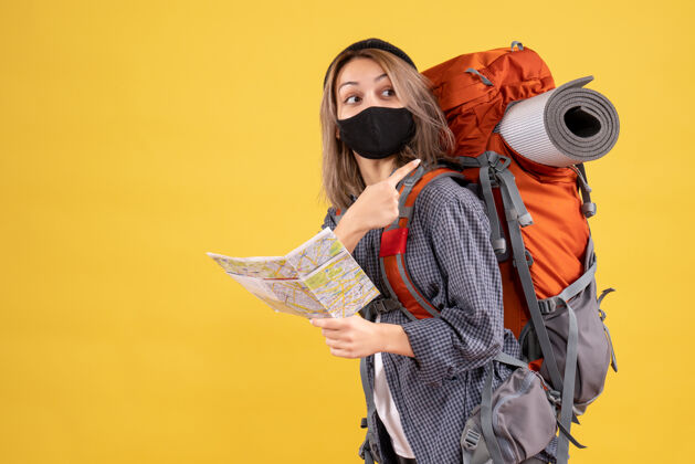 保护带着黑色面具的旅行女孩拿着地图指着背包肖像面具服装