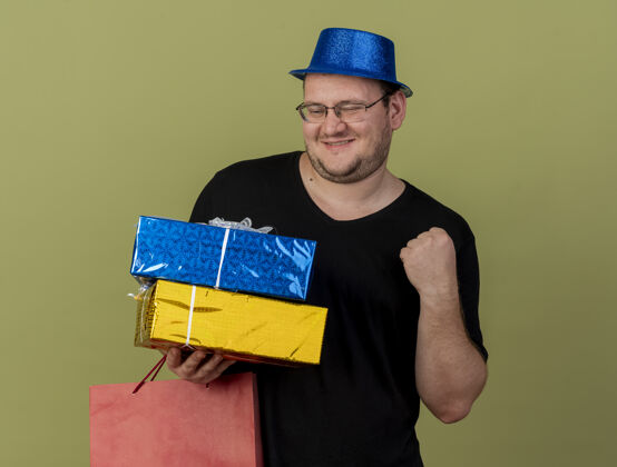 眼镜高兴的成年斯拉夫人戴着眼镜 戴着蓝色派对帽 手拿礼品盒和纸购物袋保留空间穿