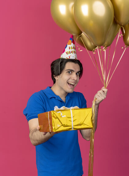 气球高加索帅哥戴着生日帽 手里拿着氦气球和礼盒复制兴奋礼物