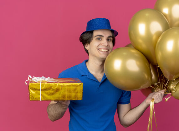 礼物面带微笑的白人帅哥头戴蓝色派对帽手持氦气球和礼盒气球穿帽子