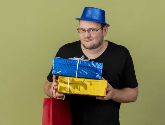 帽子兴奋的成年斯拉夫人戴着眼镜 戴着蓝色派对帽 手里拿着礼品盒和纸购物袋纸张穿蓝色