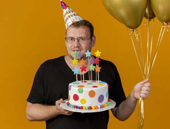 男人自信的成年斯拉夫人戴着眼镜 戴着生日帽 手里拿着氦气球和生日蛋糕眼镜光学气球