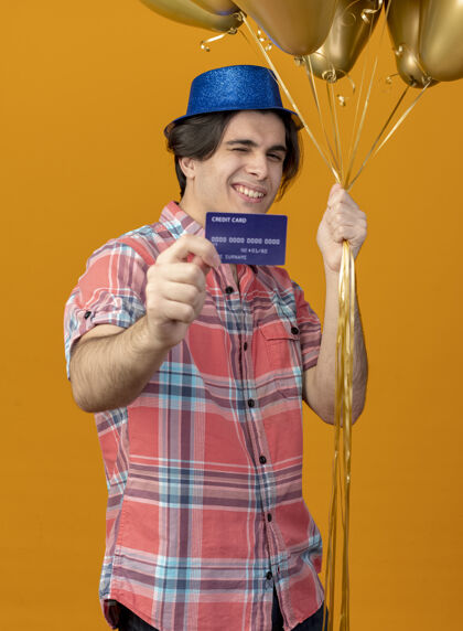 蓝色微笑自信的白人帅哥头戴蓝色派对帽手持氦气球和信用卡气球太空派对