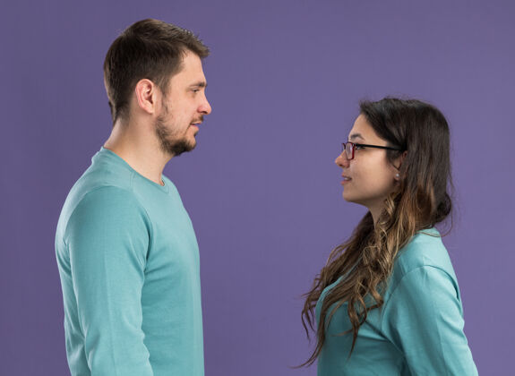 年轻年轻漂亮的情侣穿着蓝色休闲服快乐开朗的男人和女人站在紫色的墙上看着彼此相爱快乐女人站立欢呼