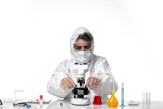 视图男医生穿着防护服 戴着口罩 用显微镜观察浅白色医学男性医生