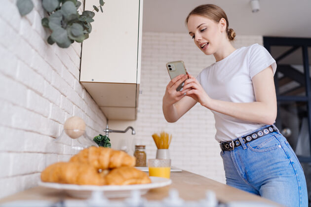 微笑年轻美女用手机拍牛角包舒适女性厨房