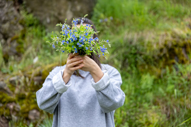 天女孩把脸藏在森林里采来的一束鲜花后面蓝色女人女人