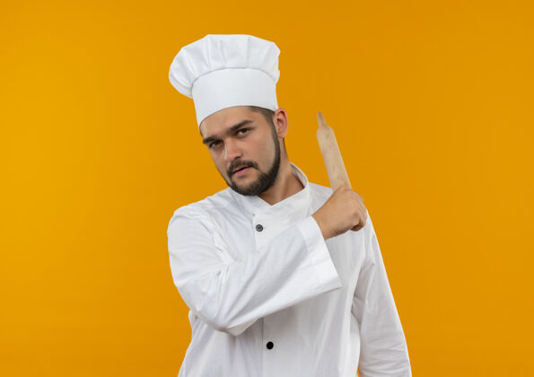 指点自信的年轻男性厨师 身着厨师制服 指着身后 橙色墙壁上的擀面杖 留有复制空间男性滚自信