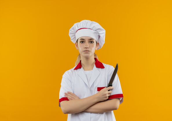 烹饪自信的年轻漂亮厨师身着厨师制服 站在封闭的姿势和持刀隔离在橙色墙上的复制空间信心漂亮持有