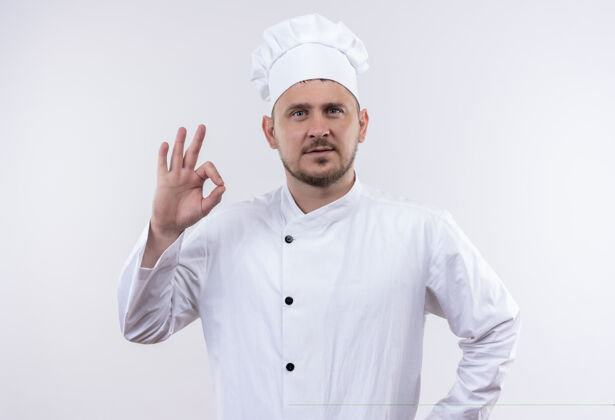 年轻自信的年轻帅哥厨师身着厨师制服 在白墙上做着“ok”的招牌制服自信烹饪