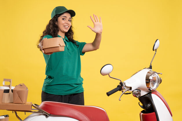 送货正面图身着绿色制服的女快递员 黄色背景上有一个小食品包 工作颜色为工作递送女服务人员食品球员女信使成人