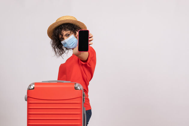 成人正面图年轻女性戴着红包 戴着口罩拿着手机 背景是白色的太阳冠状病毒大流行旅游病毒颜色肖像旅行面具
