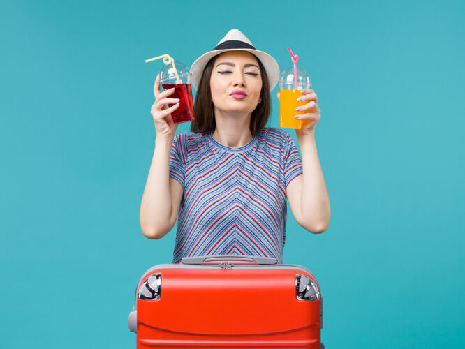 果汁正面图：度假妇女手持新鲜果汁在蓝色背景的海面上乘机旅行航行举行美丽
