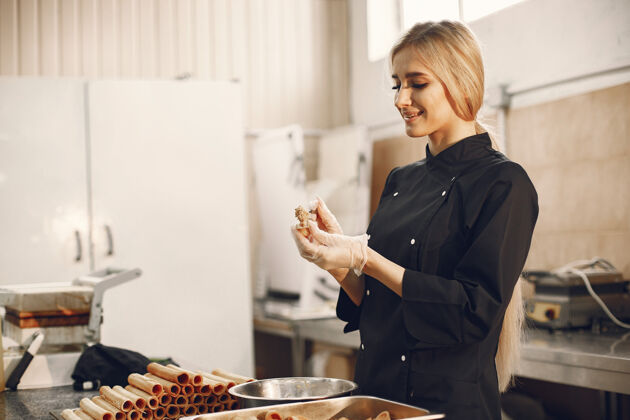 准备穿着黑色制服的金发女郎在餐厅的厨房里准备着不同的糖果和饼干成人面包房烹饪