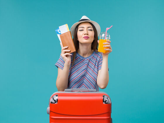 航行前景度假的女人拿着她的果汁和机票在蓝色的书桌上旅行夏天旅行度假海上微笑举行果汁