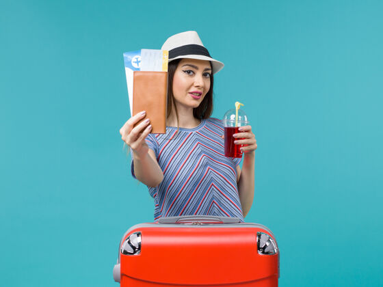 旅程前视女子在度假 手持红包和红汁 在蓝色背景下乘船远航 女子度假果汁航行票