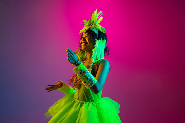 威尼斯人美丽的年轻女子在狂欢节 时尚的化装舞会服装与羽毛跳舞的梯度墙上霓虹灯化妆舞会节日狂欢节