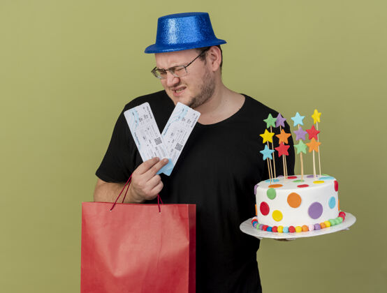 纸张戴着眼镜 戴着蓝色派对帽 拿着纸购物袋 生日蛋糕和机票的未租成年斯拉夫男子不愉快购物机票